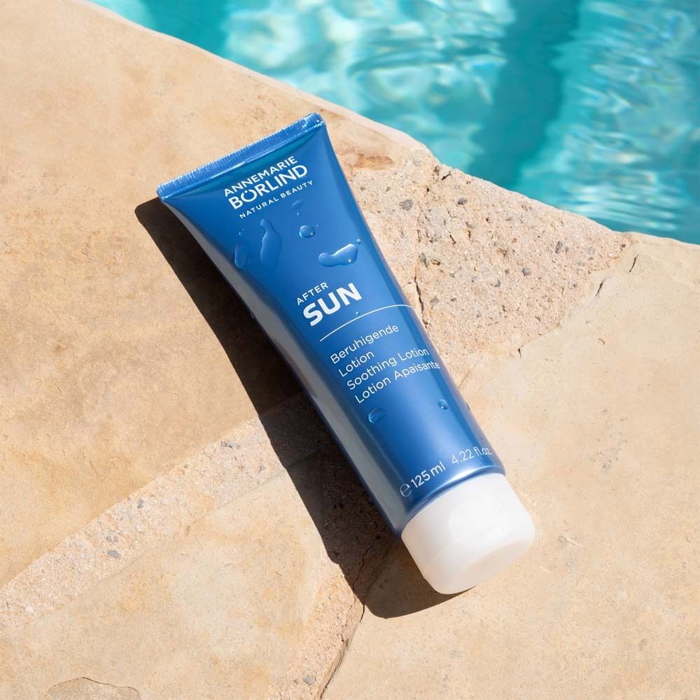 Blaue Tube mit weißem Deckel am Poolrand. Aufschrift: AFTER SUN, Beruhigende Lotion. Wasser im Hintergrund.