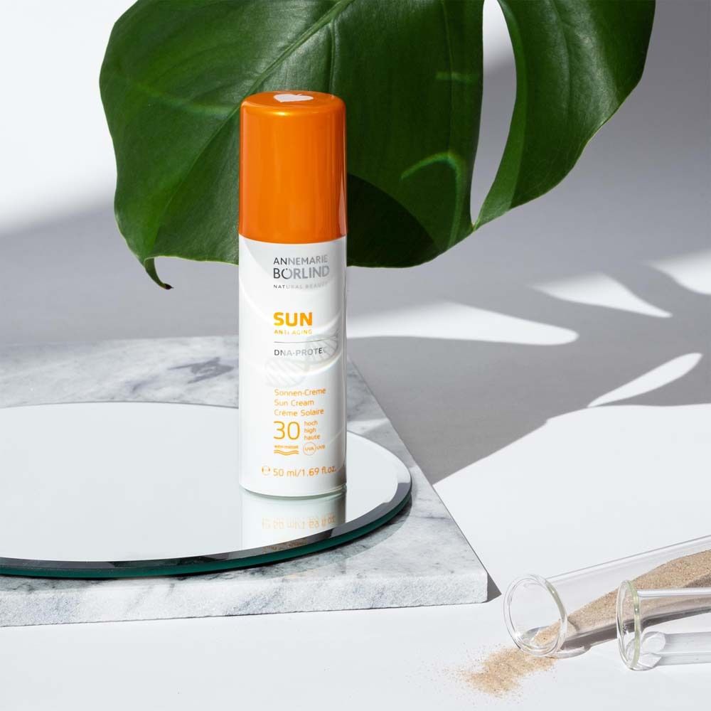 Sonnencreme-Tube mit orangefarbenem Deckel auf Spiegel und Blatt. Text: ANNEMARIE BÖRLIND, SUN, LSF 30.