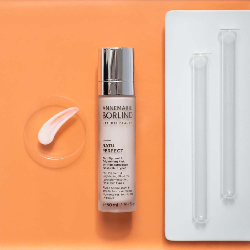 ANNEMARIE BÖRLIND NATU PERFECT Fluid mit Zubehör. Rosa Fluid, Glasplatte, 2 Röhrchen. Auf orangefarbenem Hintergrund.