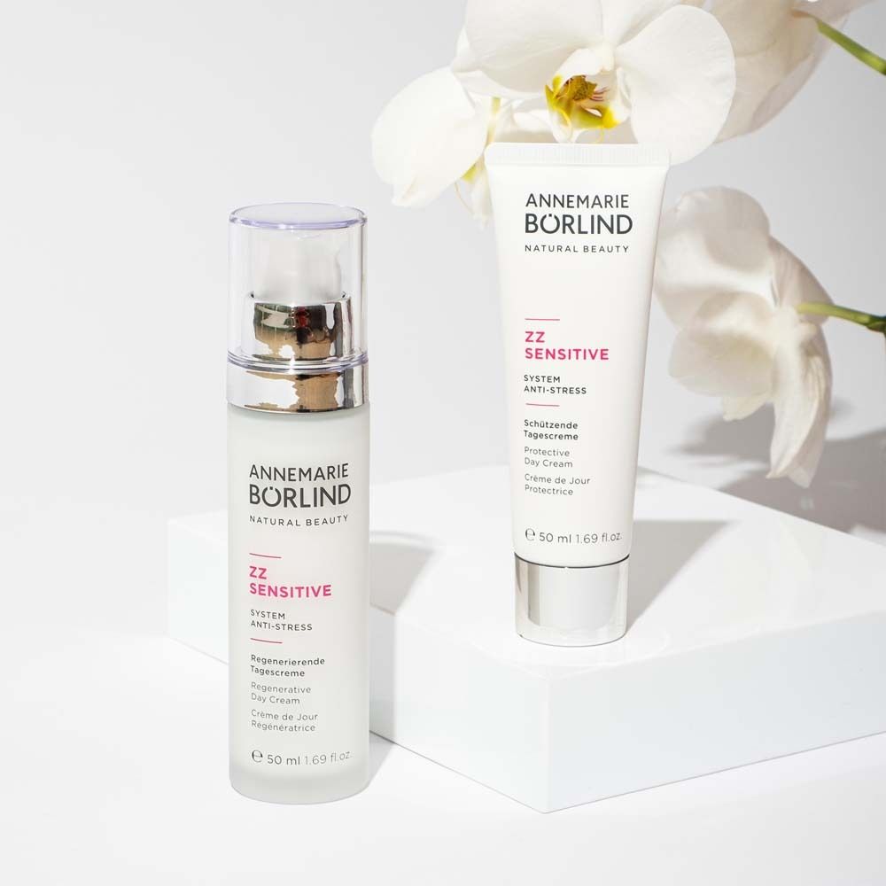 Zwei Produkte: Creme-Flasche und Tube. Aufschrift: ANNEMARIE BÖRLIND, ZZ SENSITIVE. Weiße Oberfläche mit Orchideen.