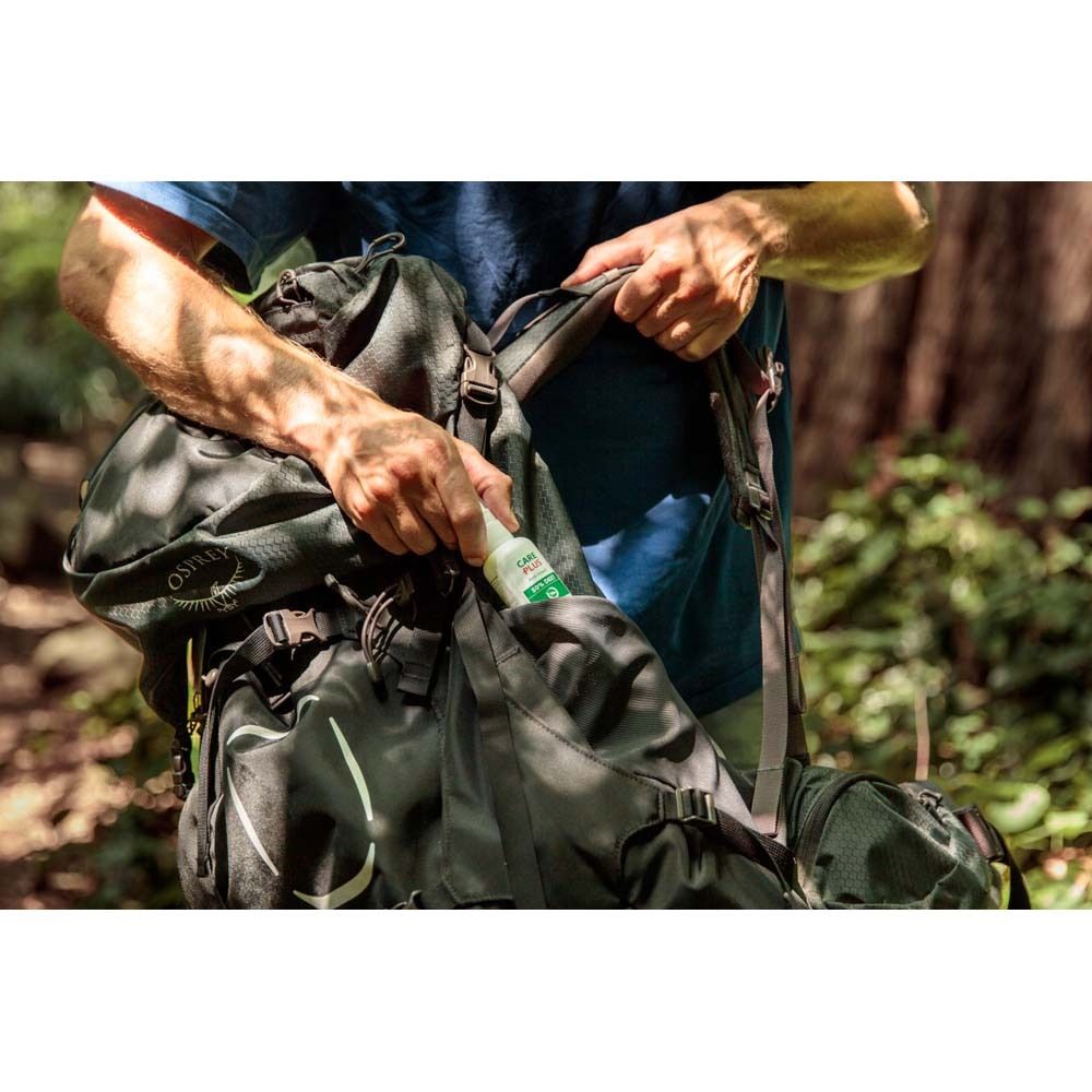 Eine Person verstaut eine weiße Care Plus Sprayflasche in einem Rucksack.