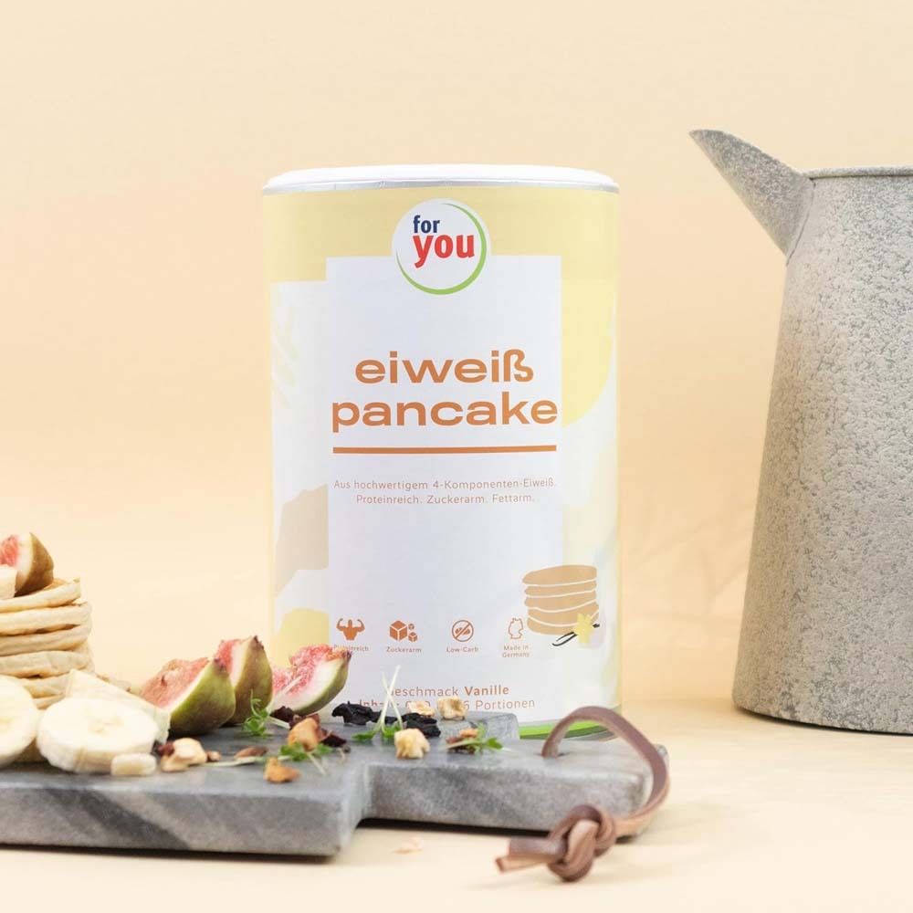 Dose "for you" Eiweiß Pancake Vanille neben Obst und Pfannkuchen. Aufschrift: "eiweiß pancake". Auf einem Brett angerichtet.