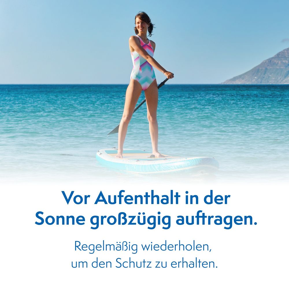 Frau auf Surfbrett im Meer. Text: Vor Aufenthalt in der Sonne großzügig auftragen. Regelmäßig wiederholen, um den Schutz zu erhalten.