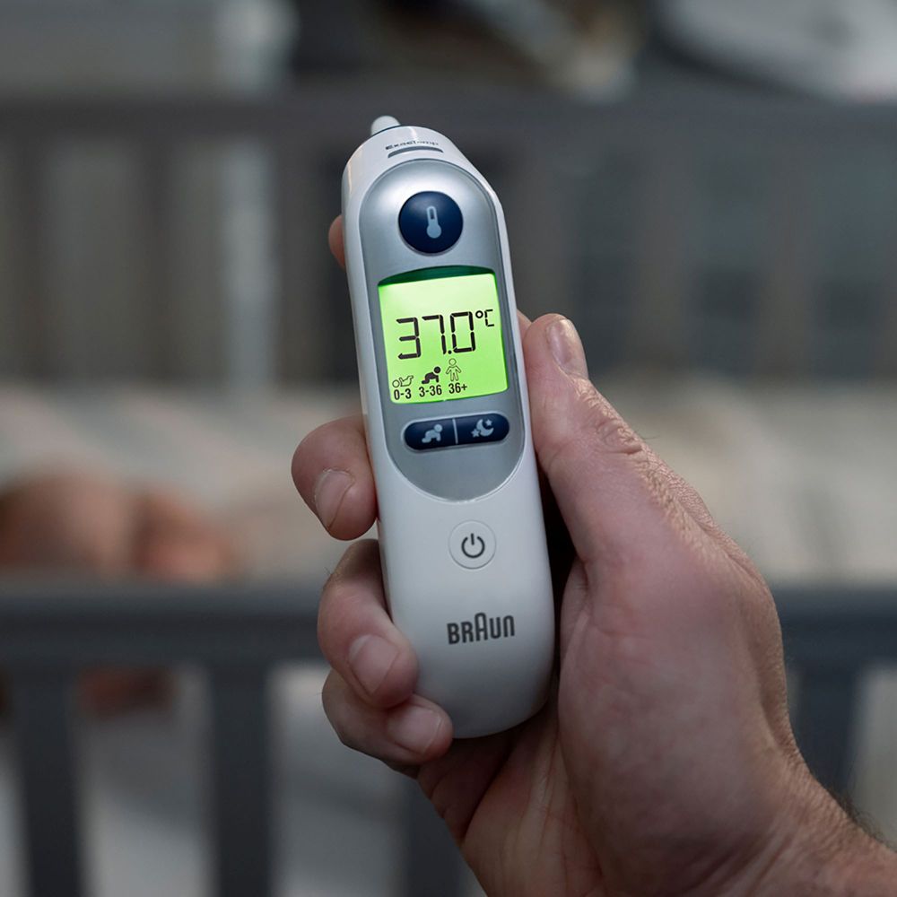 Ein Mann hält ein weißes Ohrthermometer Braun ThermoScan 7+ in der Hand. Digitalanzeige mit Temperatur.