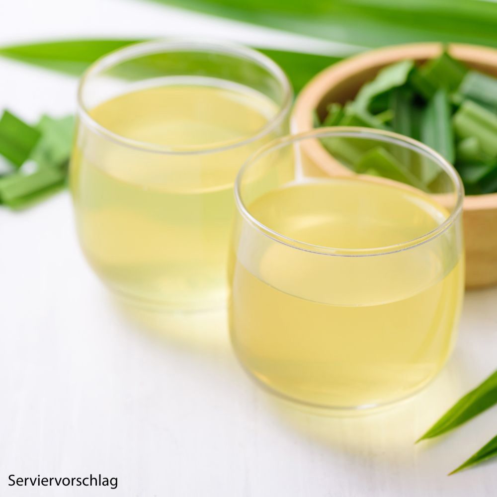 Zwei Gläser mit gelbem Getränk. Grüne Blätter und Holzschale daneben. Servierbeispiel.