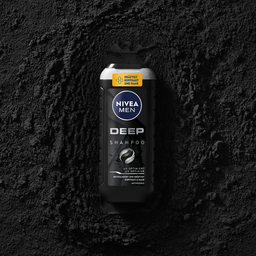 NIVEA MEN DEEP Shampoo Flasche liegt inmitten von schwarzem Pulver, das Aktivkohle symbolisiert.