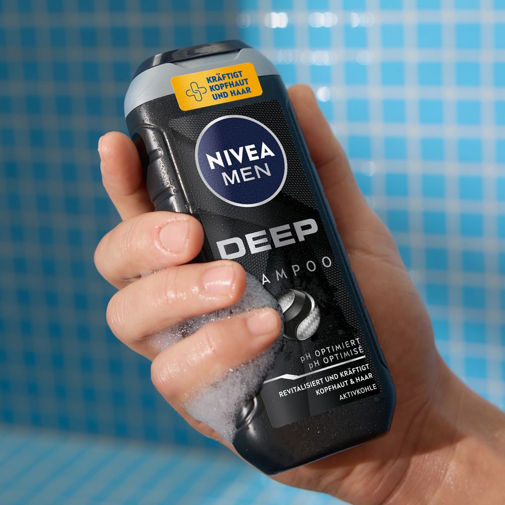 Hand hält NIVEA MEN DEEP Shampoo Flasche mit Schaum. pH-optimiert mit Aktivkohle.