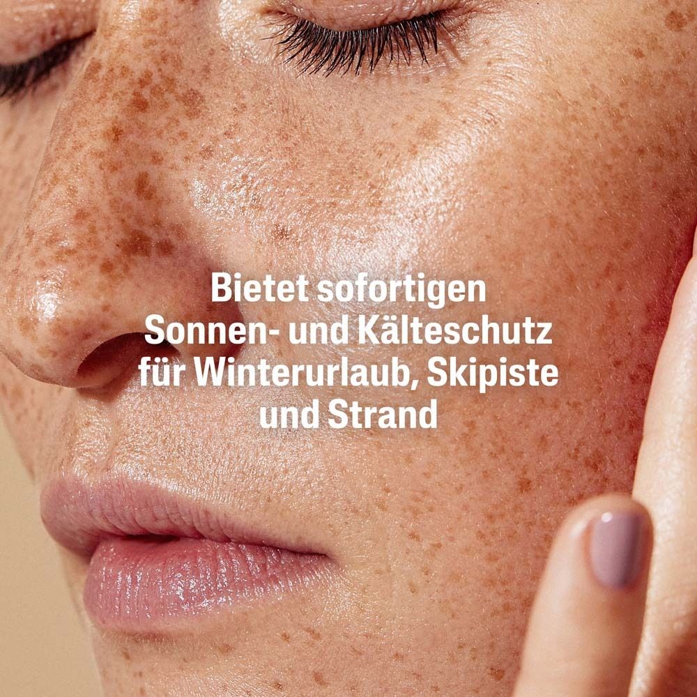 Gesicht einer Frau. Text: Sofortiger Sonnen- und Kälteschutz für Winterurlaub, Skipiste und Strand.
