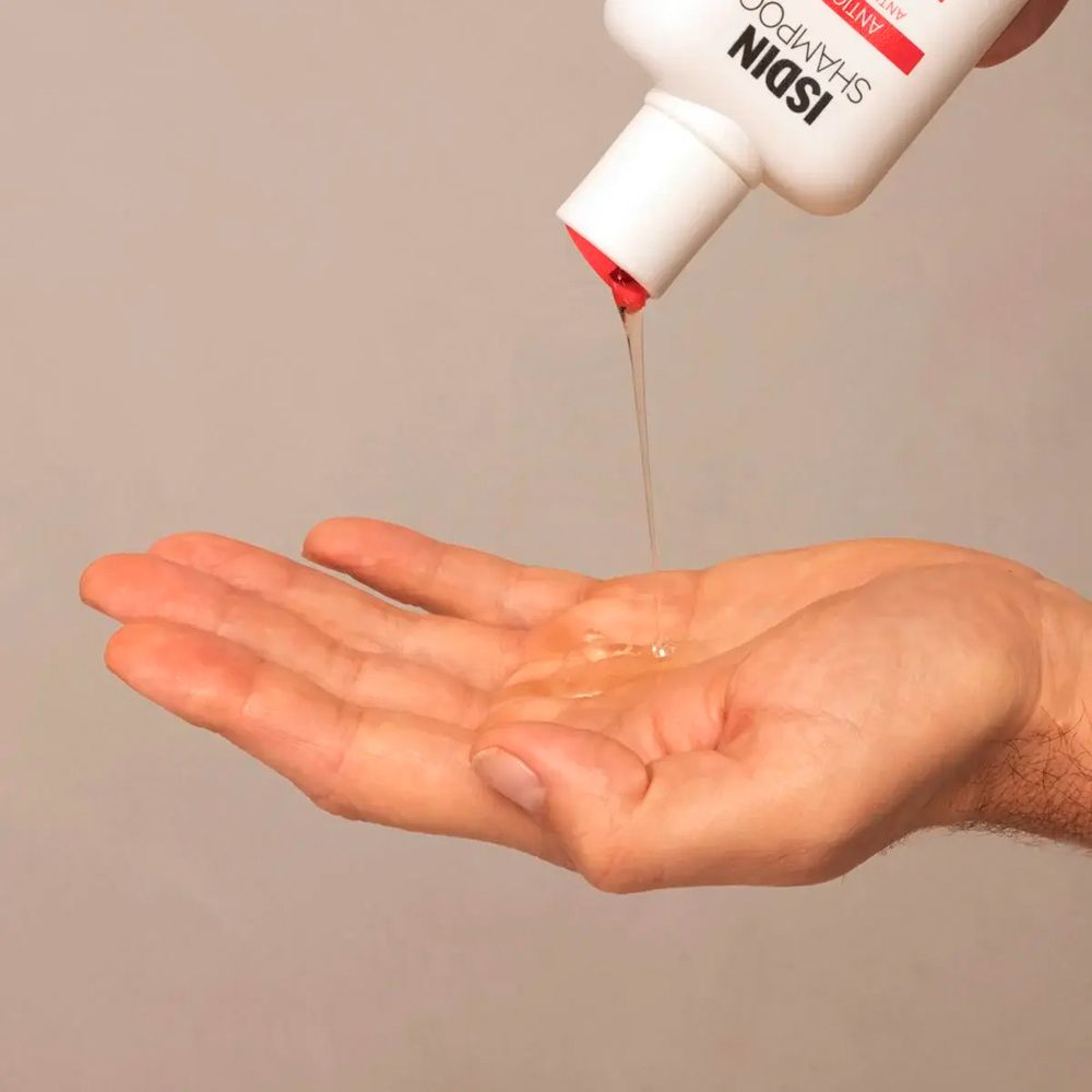 Shampoo wird in eine Hand gegossen. Flakon mit rotem Deckel. ISDIN Shampoo.