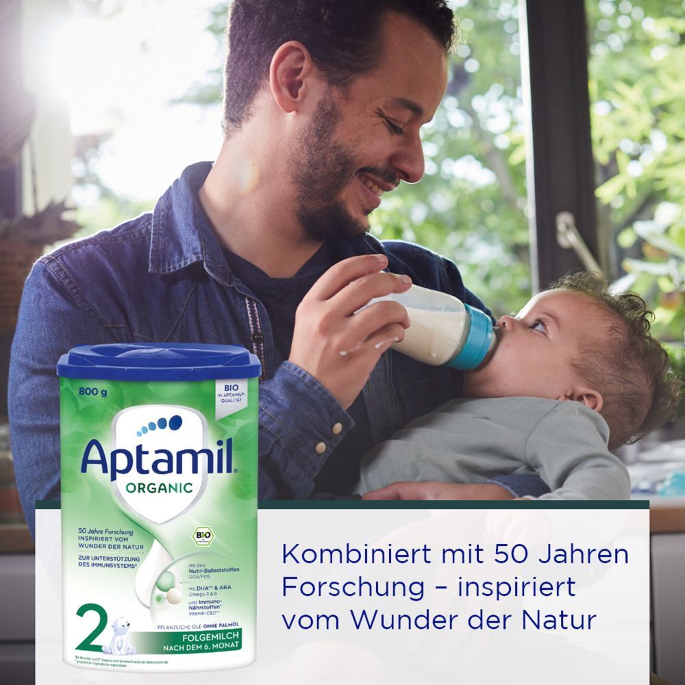 Mann füttert Baby mit Flasche. Aptamil Organic 2 Dose. Text: Inspiriert vom Wunder der Natur.