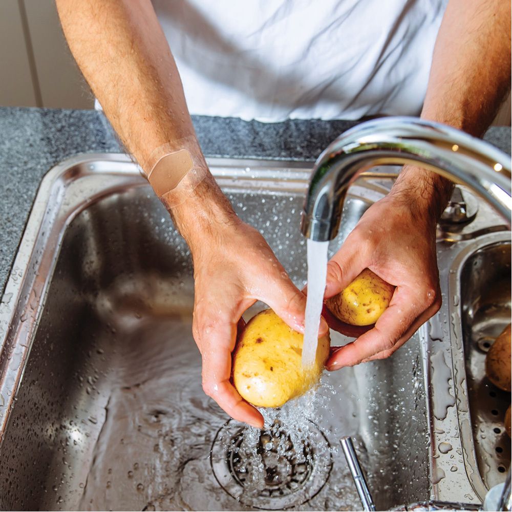 Hände waschen Kartoffeln unter fließendem Wasser. Ein Pflaster am Handgelenk.