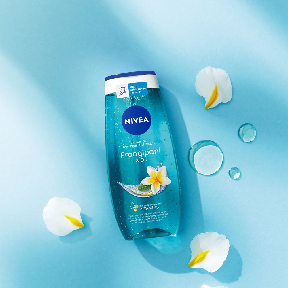 NIVEA Frangipani & Oil Pflegedusche auf blauem Hintergrund mit Blütenblättern und Wassertropfen.