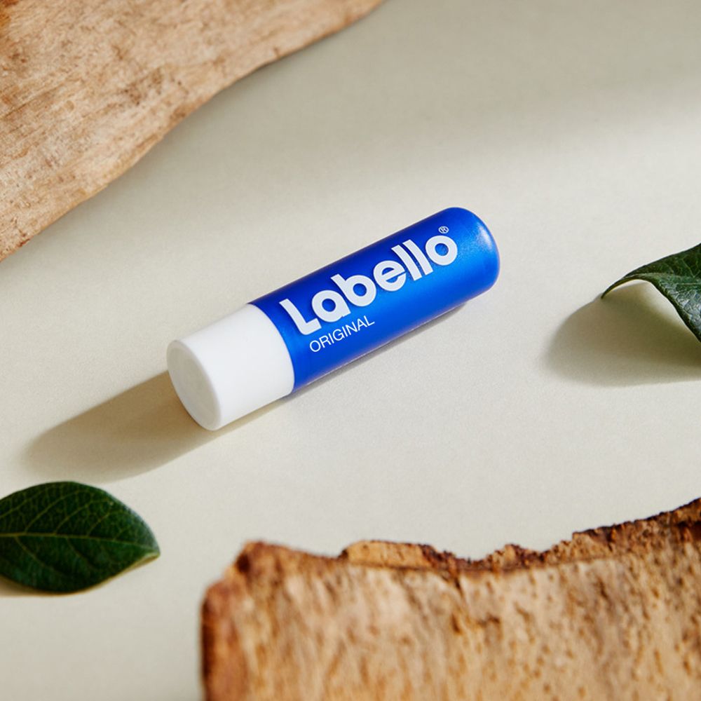 Labello Original Lippenbalsam liegt auf einer hellen Oberfläche zwischen Holz und Blättern.