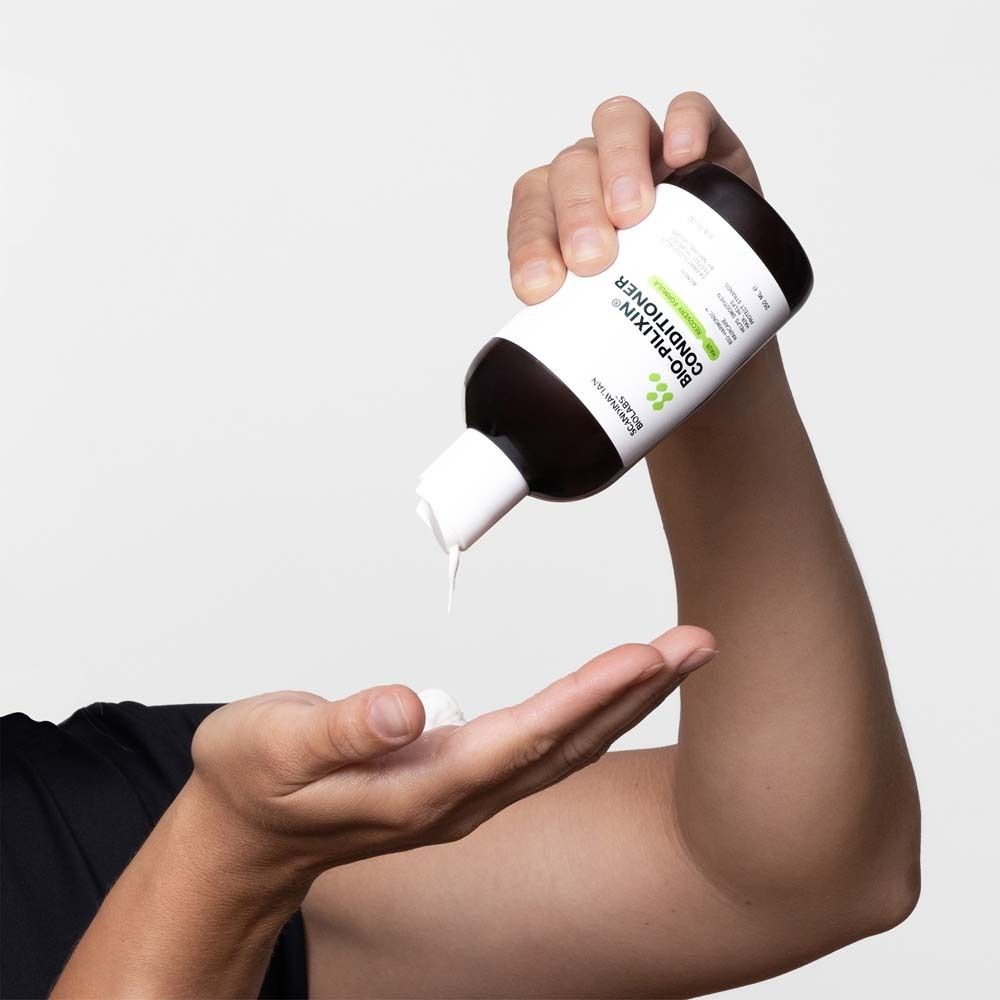 Person hält eine Flasche Conditioner. Produkt wird in die Handfläche gegossen. Schwarze Flasche mit weißem Etikett.