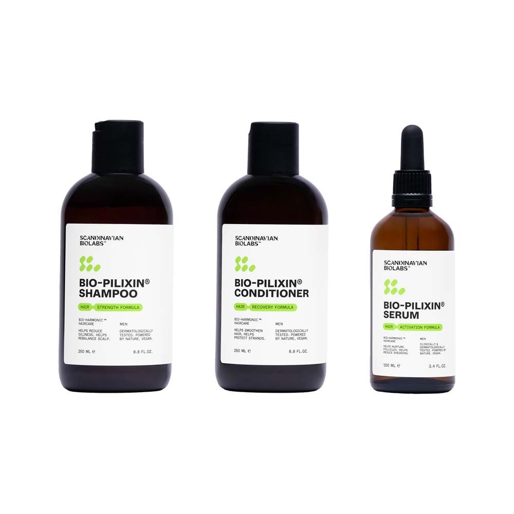 Drei Flaschen: Shampoo, Conditioner und Serum. Schwarze Kappen, braune Flaschen. Etiketten mit Text.