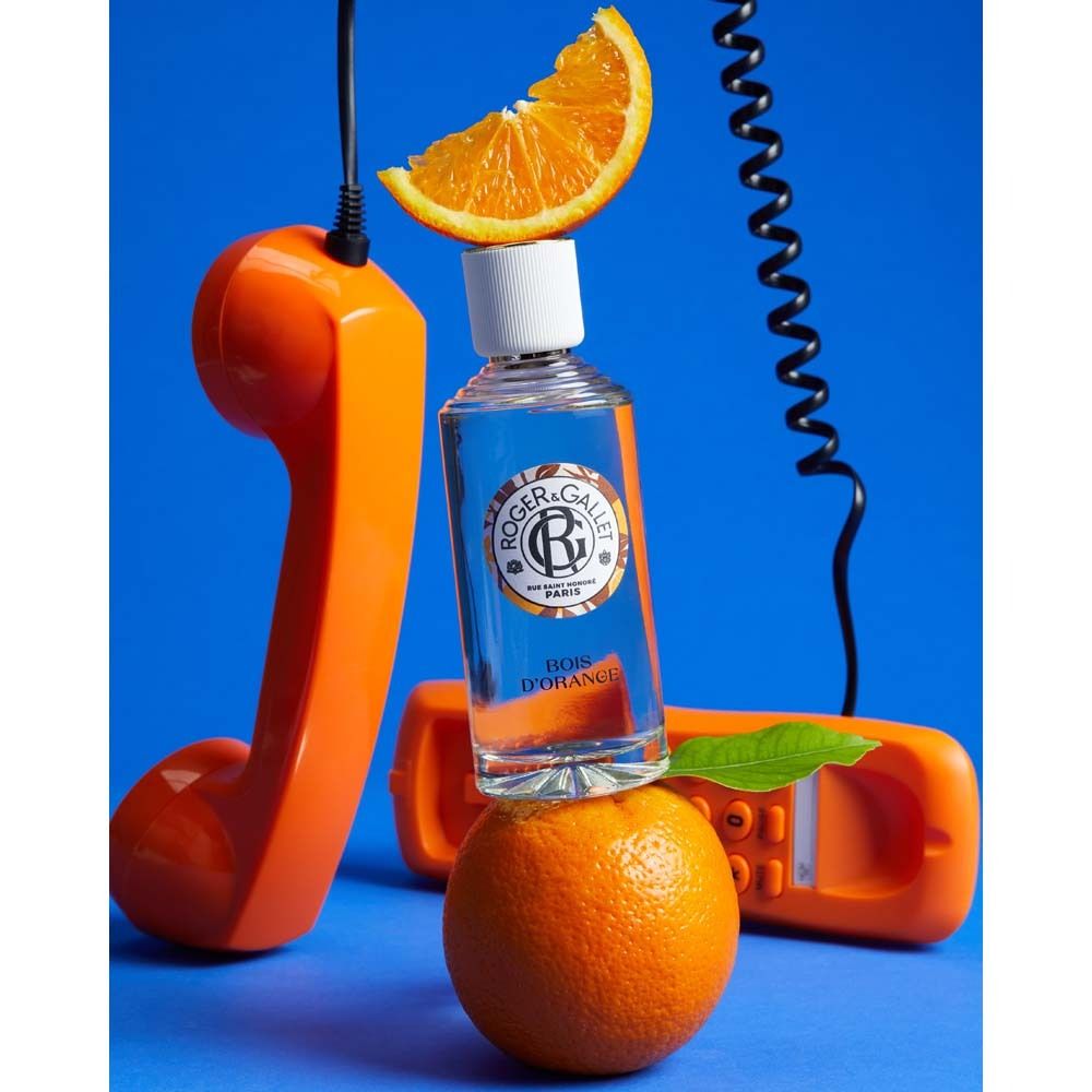 Flakon auf Orange, umgeben von Telefonhörern und Orange. Logo und Schriftzug auf dem Etikett. Aufschrift: Bois d'Orange.
