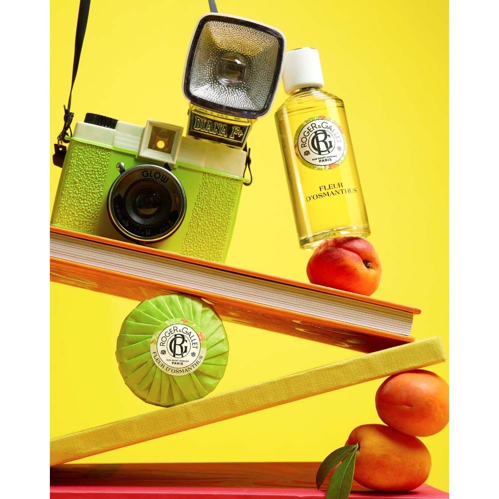 Gelbe Szene mit Kamera, Büchern, Pfirsichen und Seife. Produktflasche: Fleur d'Osmanthus.