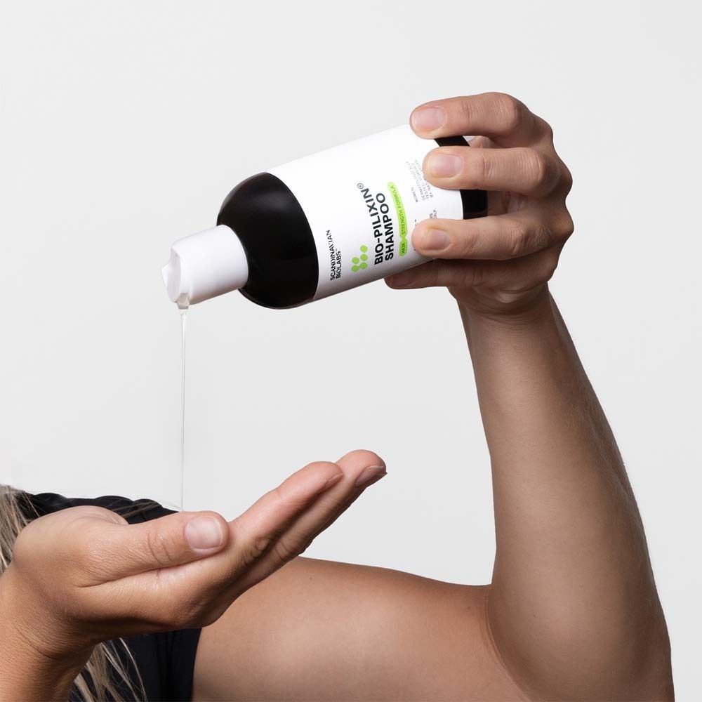 Hände halten eine Shampoo-Flasche. Flüssigkeit fließt aus der Öffnung. Aufschrift: Bio-Pilixin Shampoo.