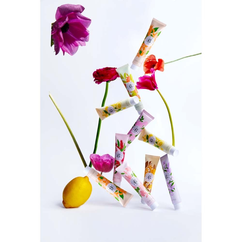 Mehrere Handcreme-Tuben mit floralen Mustern, arrangiert mit Blumen und Zitrone. Verschiedene Farben.