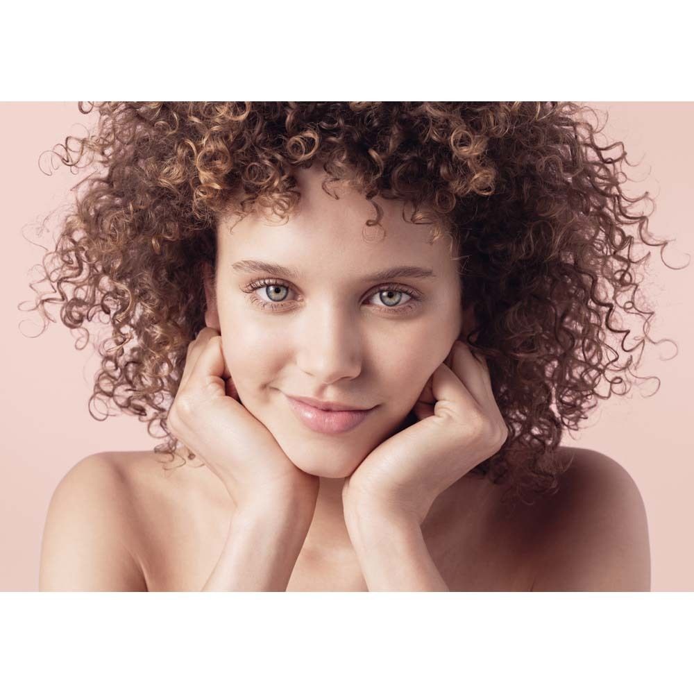 Porträt einer Frau mit lockigem Haar. Sie hält ihre Hände an ihr Gesicht. Rosa Hintergrund.