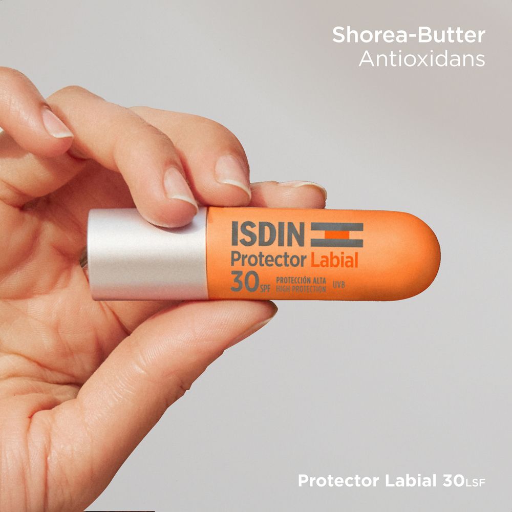 Hand hält Lippenpflegestift. Orangefarbener Deckel, silbernes Gehäuse. ISDIN Protector Labial LSF 30. Shorea-Butter.
