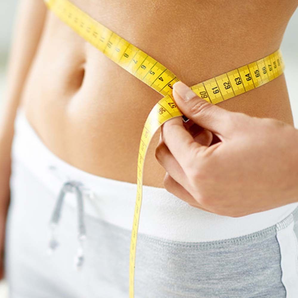 Nahaufnahme einer Person, die ihre Taille mit einem gelben Maßband misst.