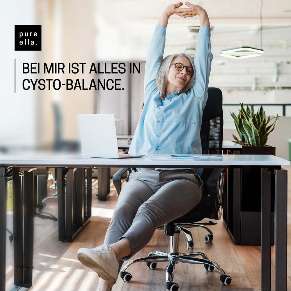 Frau sitzt am Schreibtisch, streckt Arme. Text: pure ella, Bei mir ist alles in Cysto-Balance.