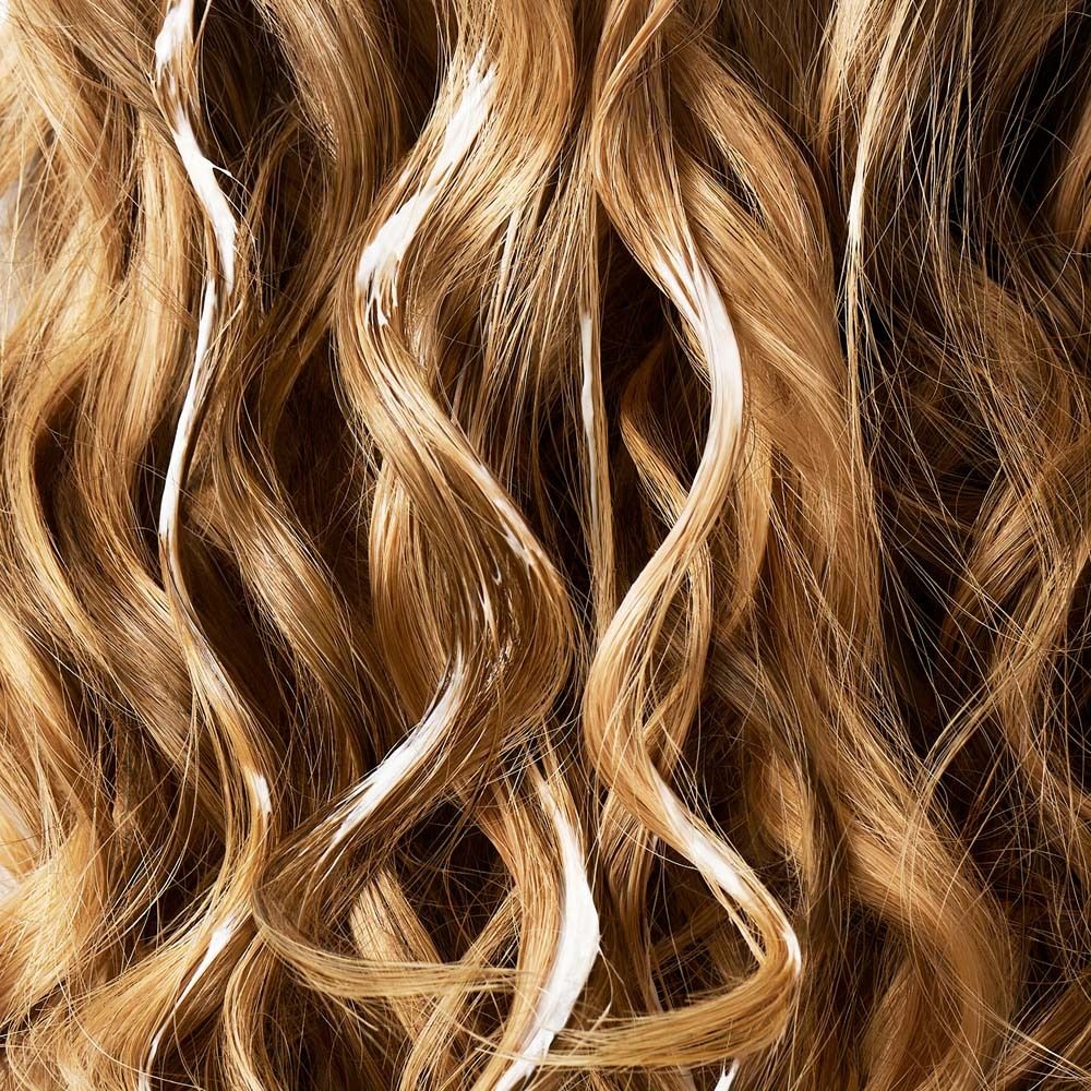 Nahaufnahme von blondem, gewelltem Haar. Strähnenweise mit weißer Creme bedeckt.