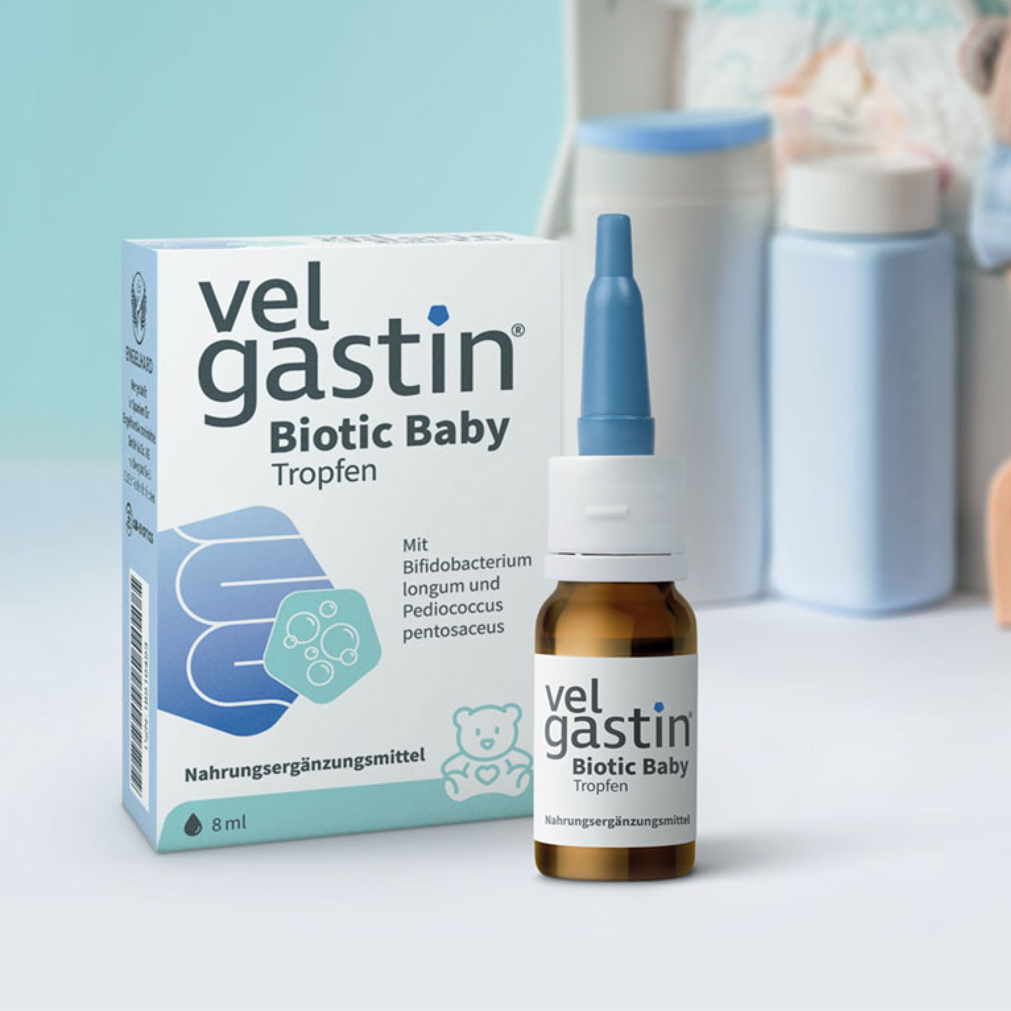 Velgastin Biotic Baby Tropfen. Flasche und Verpackung. Hintergrund mit Babyartikeln. Nahrungsergänzungsmittel.