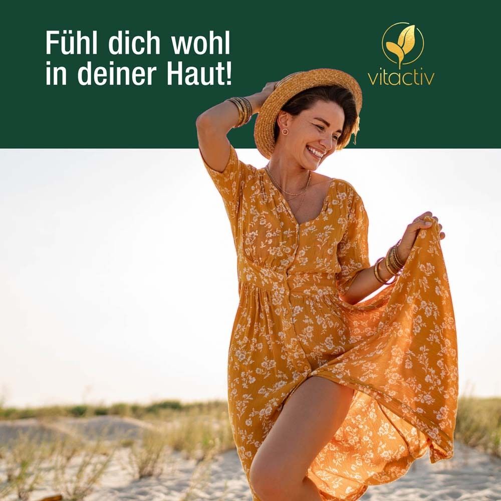 Eine Frau am Strand, die ein gelbes Kleid trägt. Sie lächelt und hält ihr Kleid.