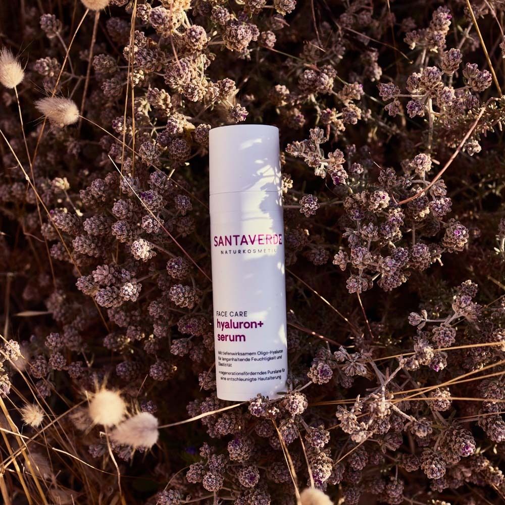 Weißer Flakon mit Produktbezeichnung, platziert in Blüten. Gesichtspflege-Serum.