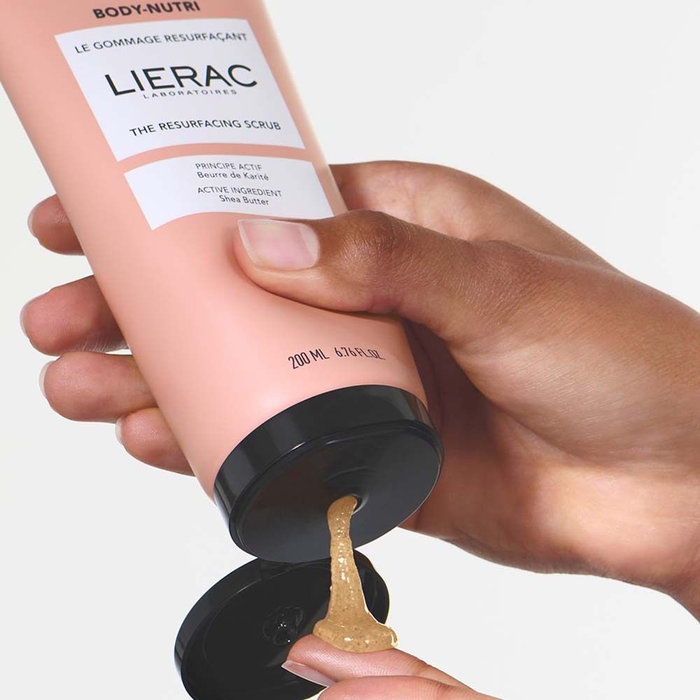 Hand drückt Peeling aus rosa Tube. Aufschrift: BODY-NUTRI, LIERAC, THE RESURFACING SCRUB.