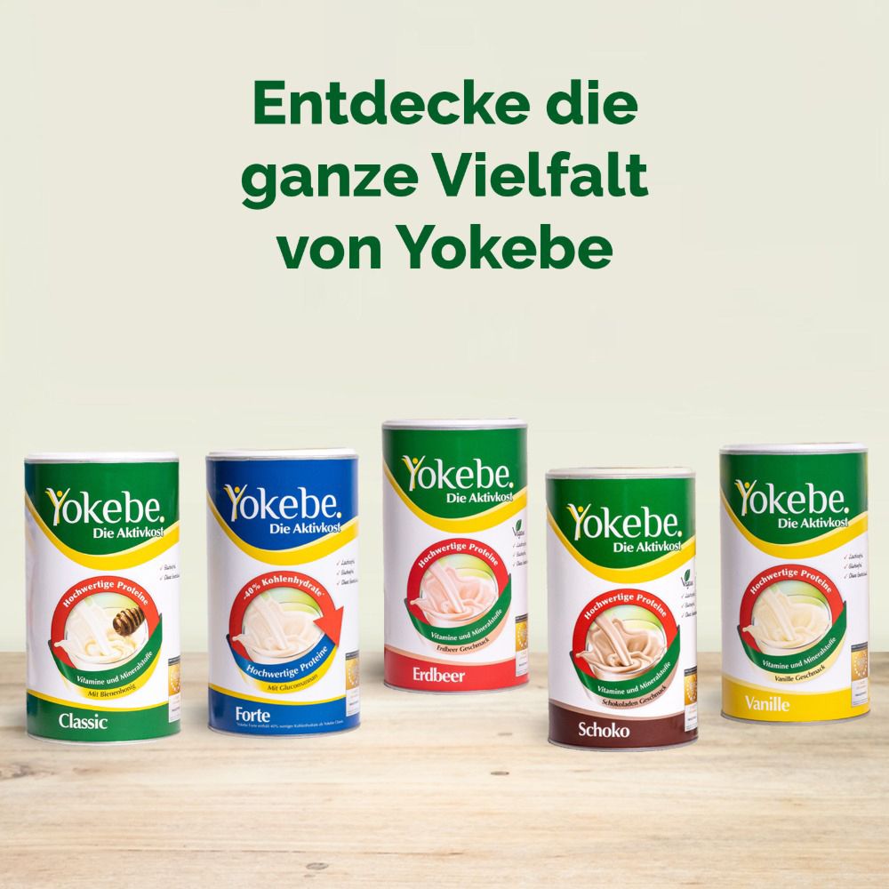 Fünf Dosen Yokebe. Sorten: Classic, Forte, Erdbeer, Schoko, Vanille. Auf Holzuntergrund. Text: Entdecke die ganze Vielfalt.