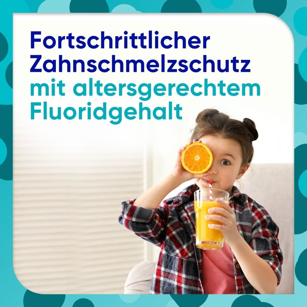 Kind hält eine Orangenscheibe vor das Auge und trinkt Orangensaft.