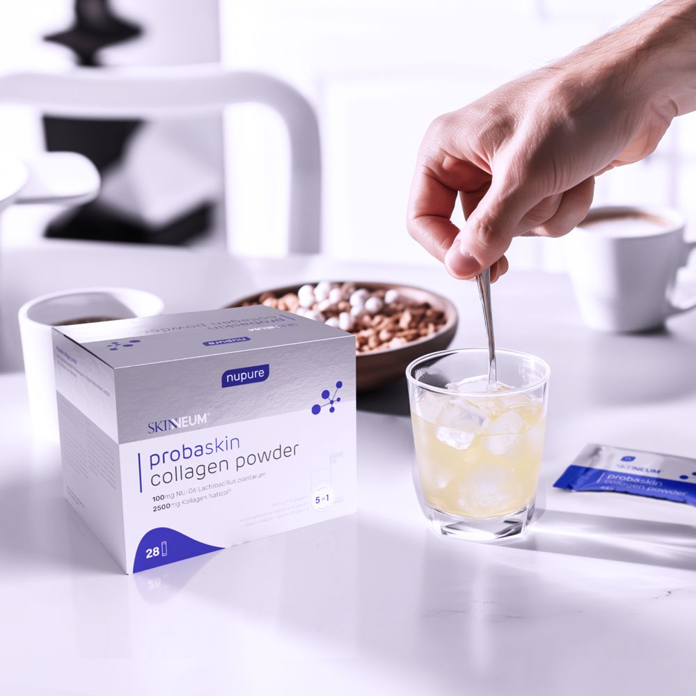 Person rührt Flüssigkeit in einem Glas. Auf dem Tisch: Produktverpackung, Beutel, Kaffeetasse, Müsli.