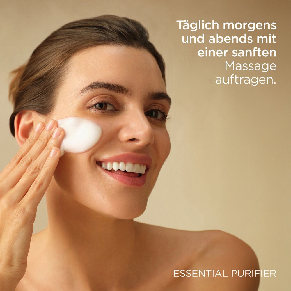 Frau trägt Schaum auf. Text: Täglich morgens und abends mit einer sanften Massage auftragen. ESSENTIAL PURIFIER.