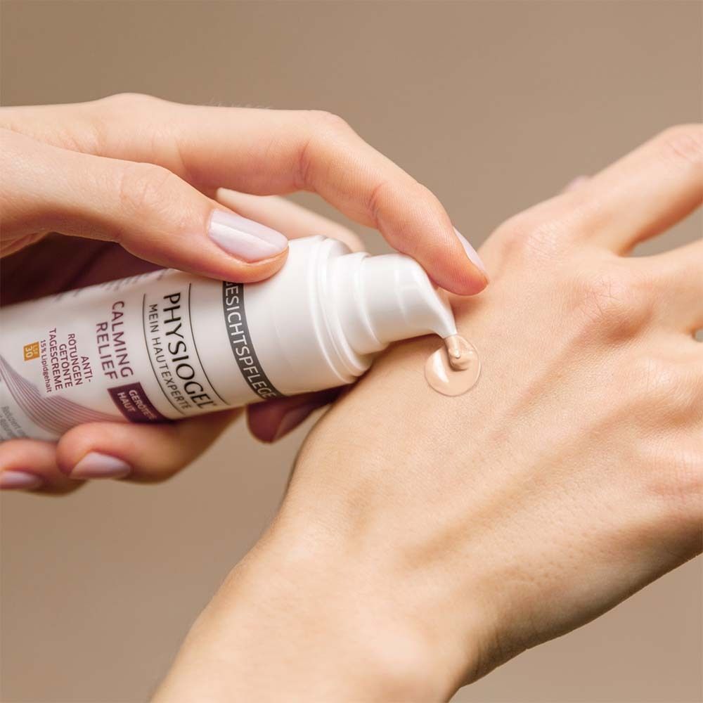 Hand mit Flasche. Creme wird auf die Hand aufgetragen. PHYSIOGEL® Calming Relief. Getönte Tagescreme.
