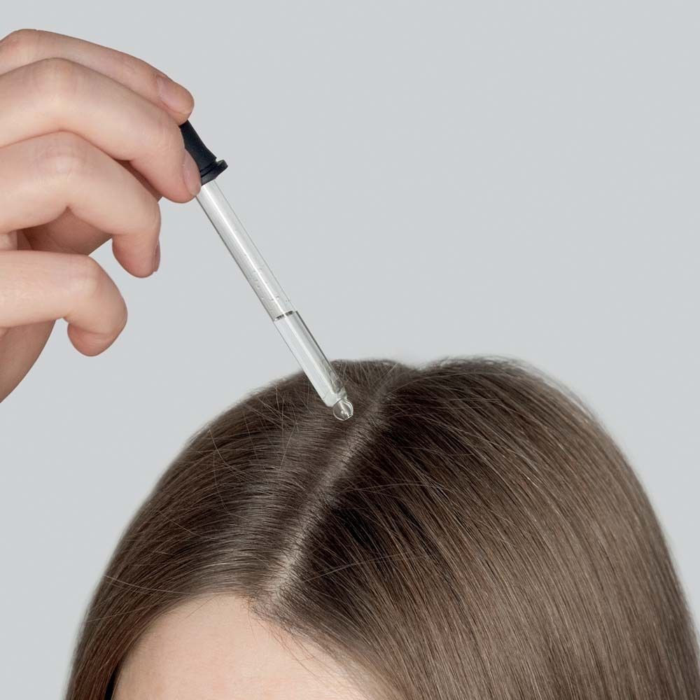 Hand mit Pipette über Kopfhaut. Tropfen fallen auf die Kopfhaut.