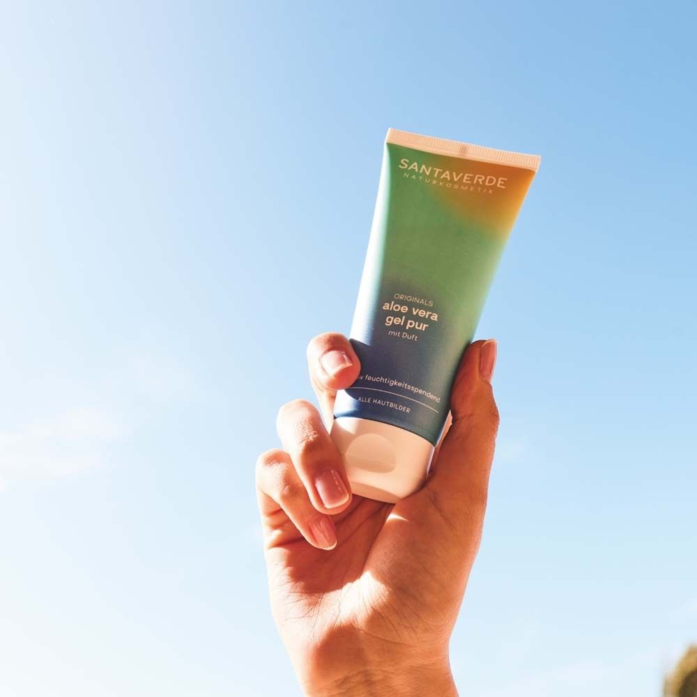 Hand hält Tube SANTAVERDE Naturkosmetik ORIGINALS aloe vera gel pur mit Duft. Blauer Himmel im Hintergrund.