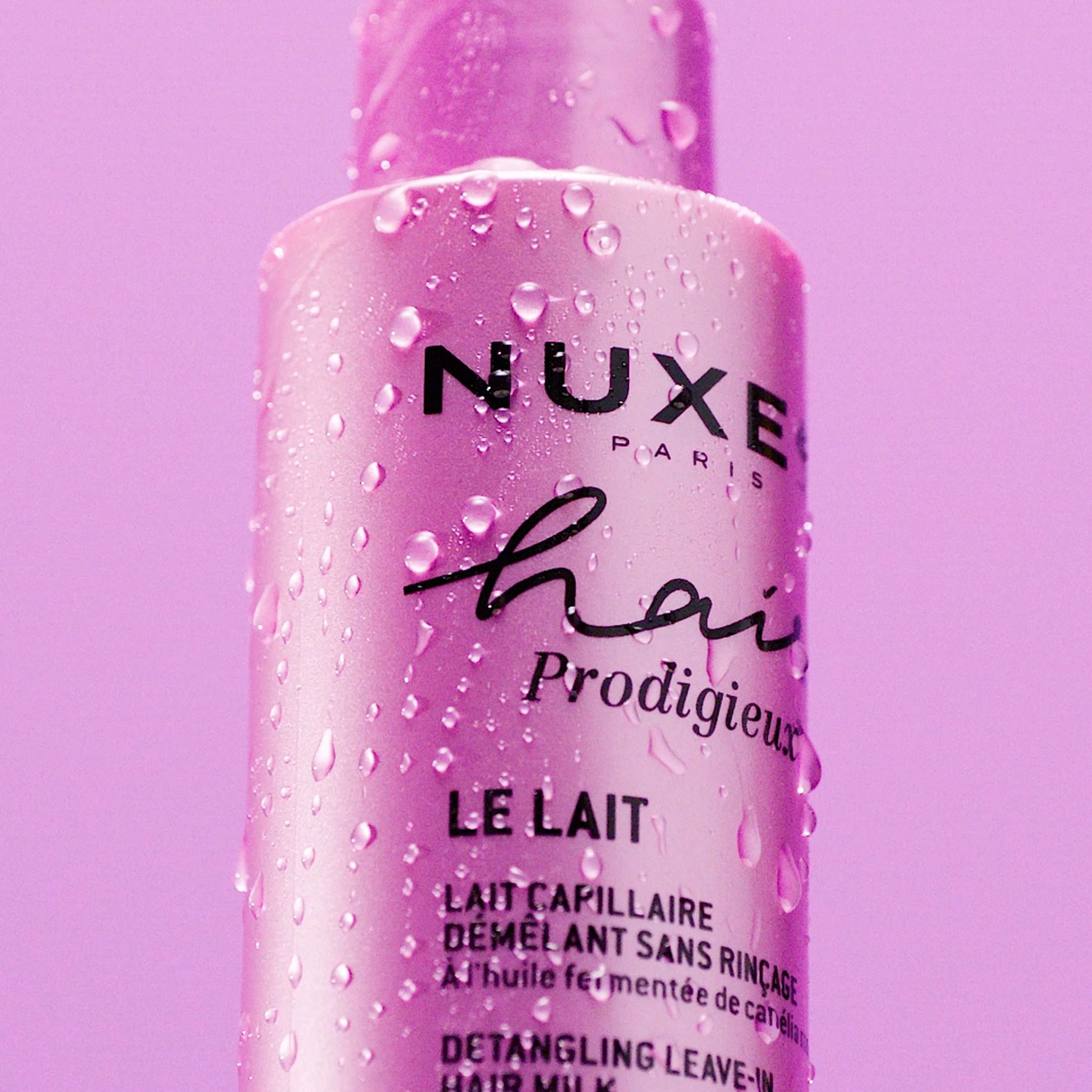 Nahaufnahme der rosa Flasche mit Wassertropfen. Aufschrift: NUXE Hair Prodigieux, Le Lait, Démêlant sans rinçage.