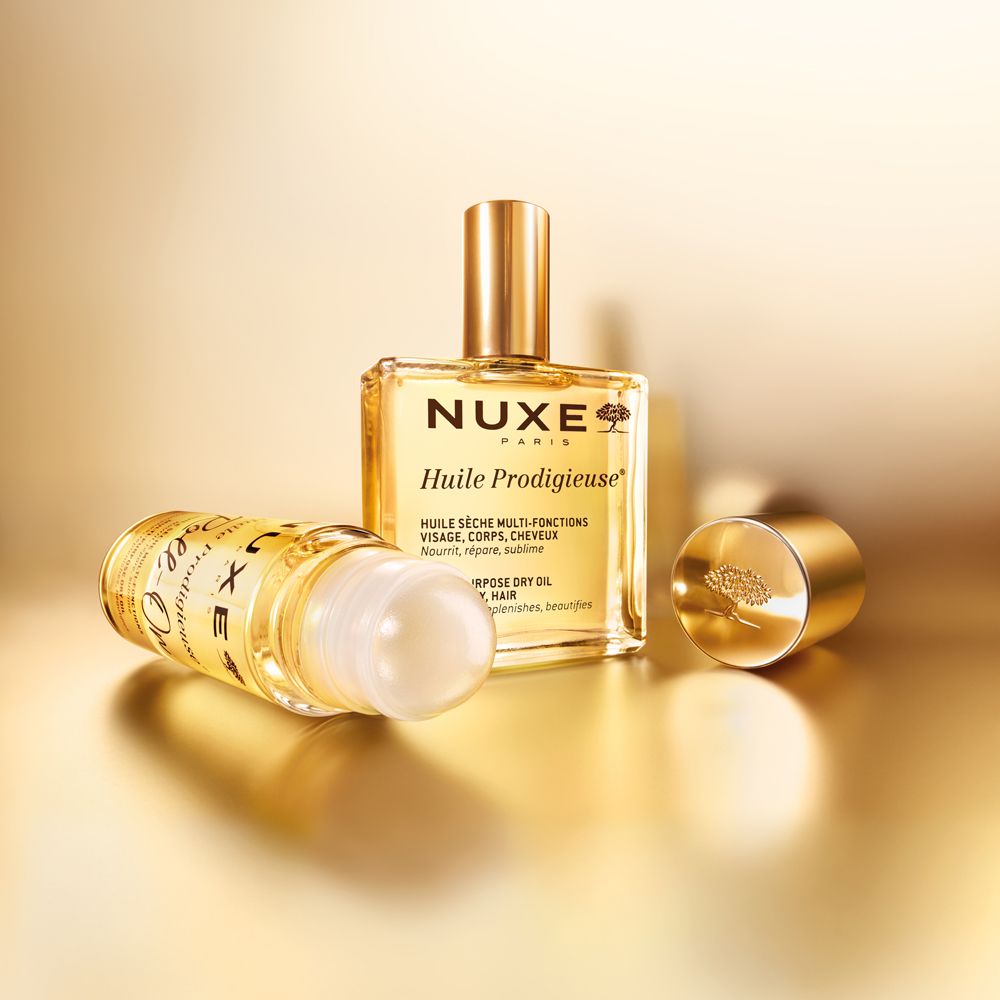 NUXE Huile Prodigieuse und Roll-on. Goldfarbene Flaschen. Offener Deckel. Goldener Hintergrund.
