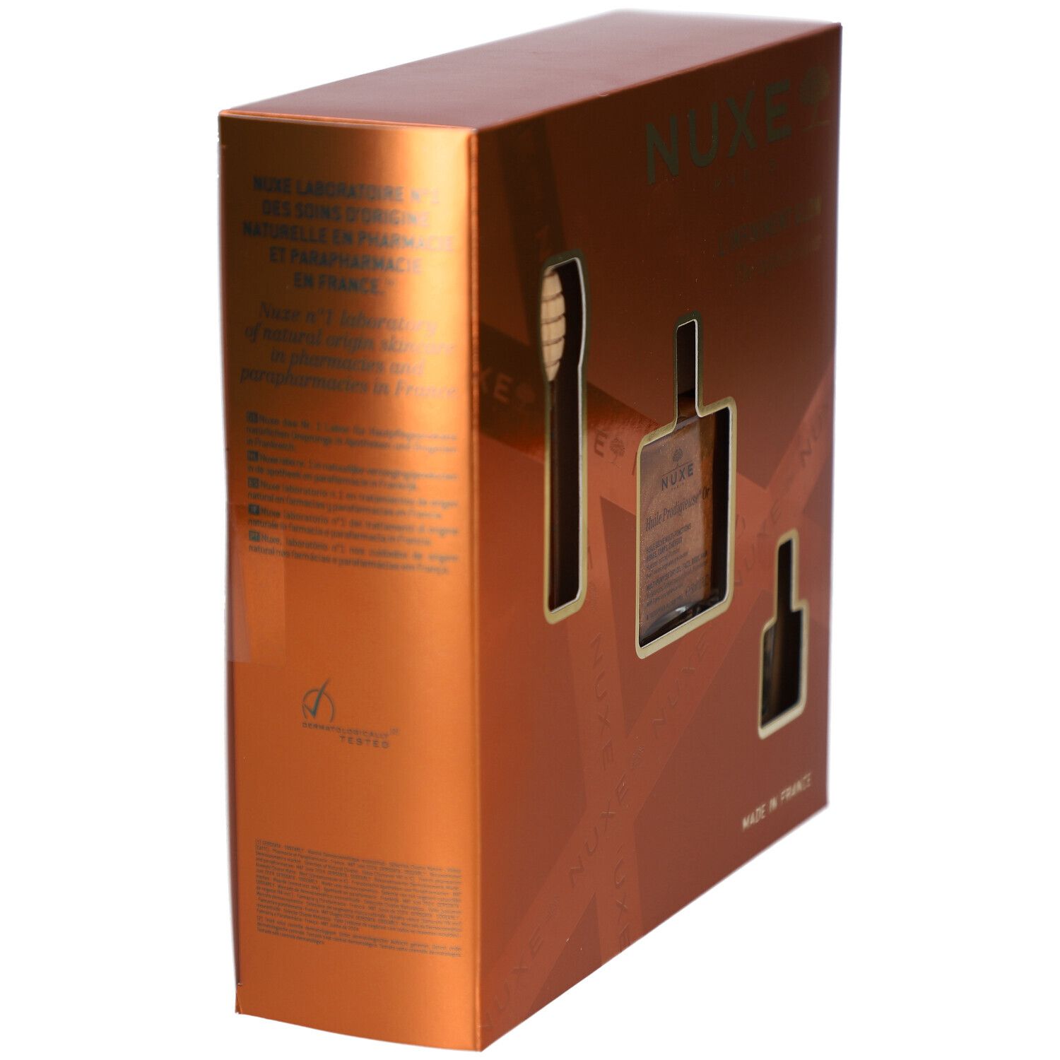 Goldfarbene Geschenkbox mit Aussparungen für Produkte. Text: NUXE, "Made in France". Seitliche Ansicht.