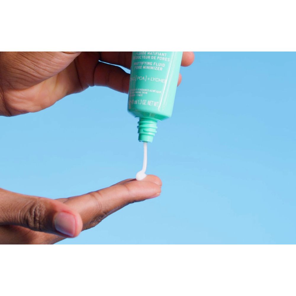 Hand drückt eine kleine Menge Fluid aus einer türkisfarbenen Tube. Fluid ist weiß.