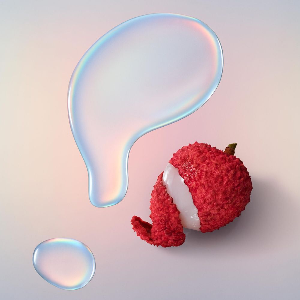 Zwei Tropfen und eine Lychee. Tropfen sind durchsichtig. Lychee ist rot und hat eine raue Oberfläche.