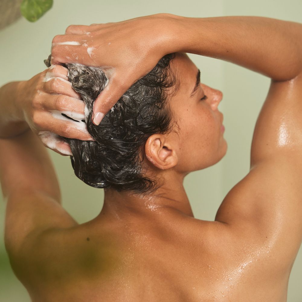 Person wäscht sich die Haare mit Shampoo. Schaum auf dem Kopf. Person mit geschlossenen Augen.