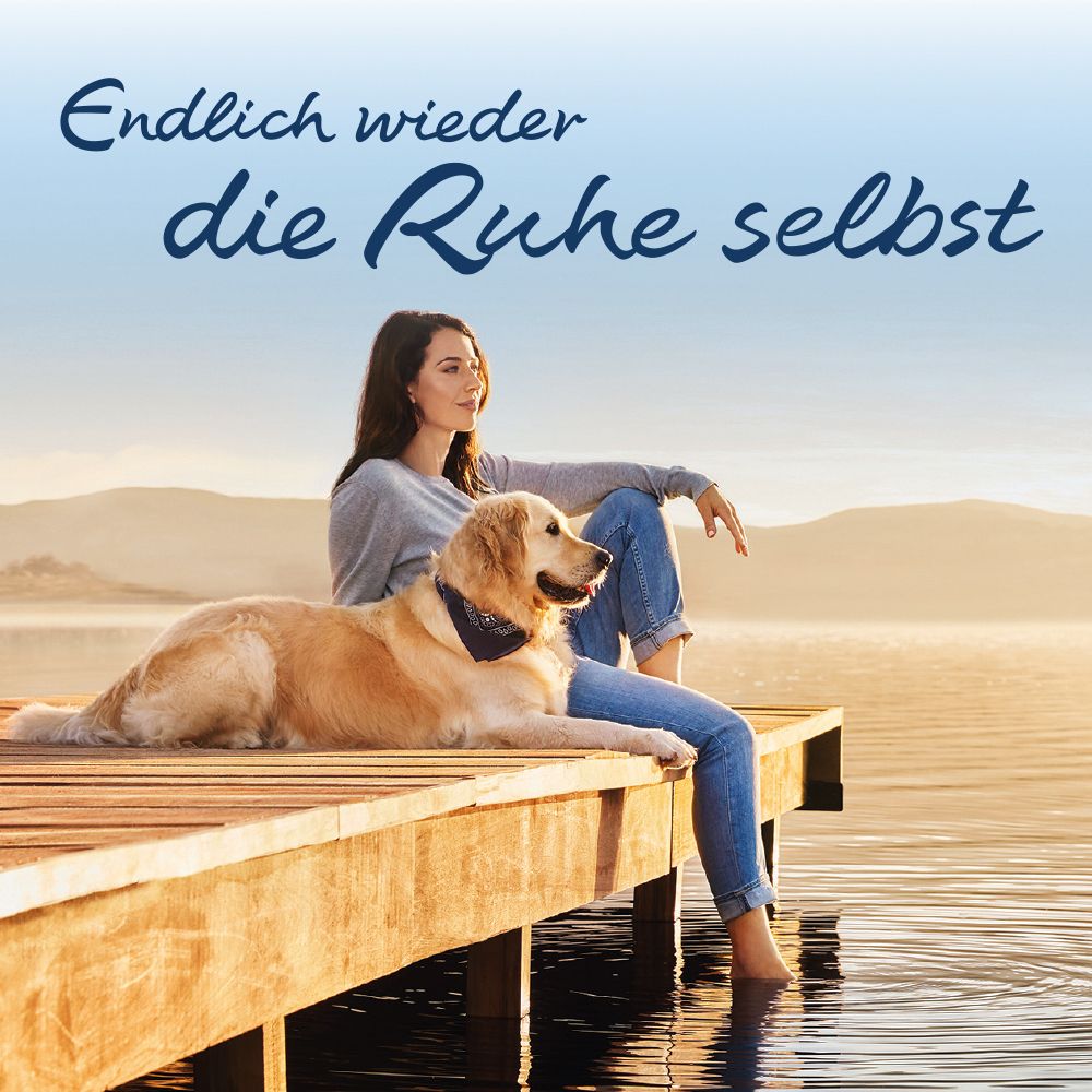 Frau sitzt auf Steg, Hund liegt daneben. Text: Endlich wieder die Ruhe selbst. See und Berge im Hintergrund.