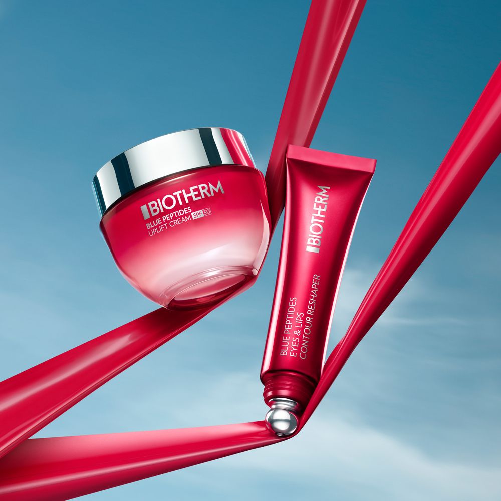 Creme und Tube. BIOTHERM Blue Peptides Eyes & Lips Reshaper. Rote Bänder im Hintergrund.