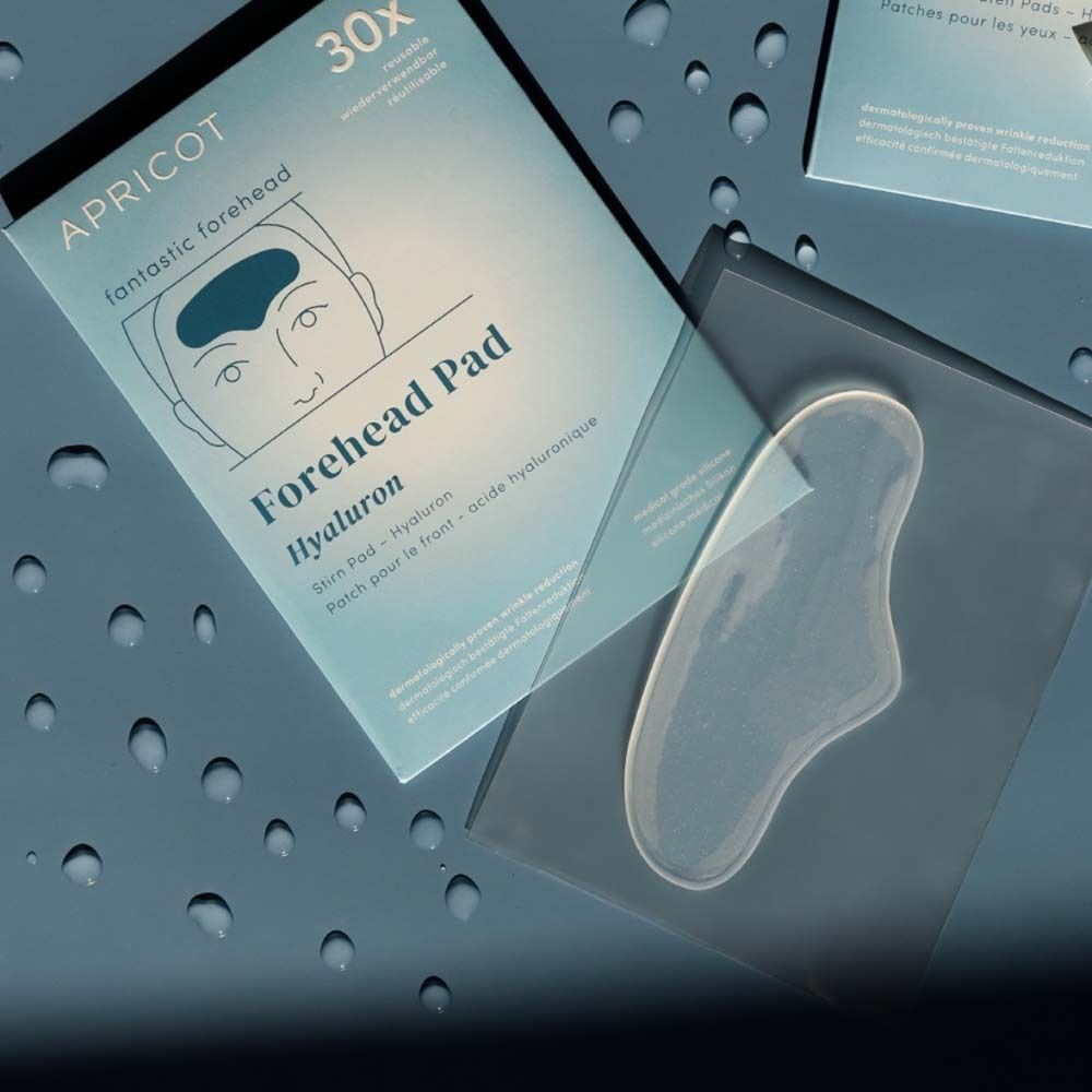 Verpackung und Stirn Pad. Marke APRICOT. Text: Forehead Pad Hyaluron. 30x. Transparentes Pad. Blauer Hintergrund.