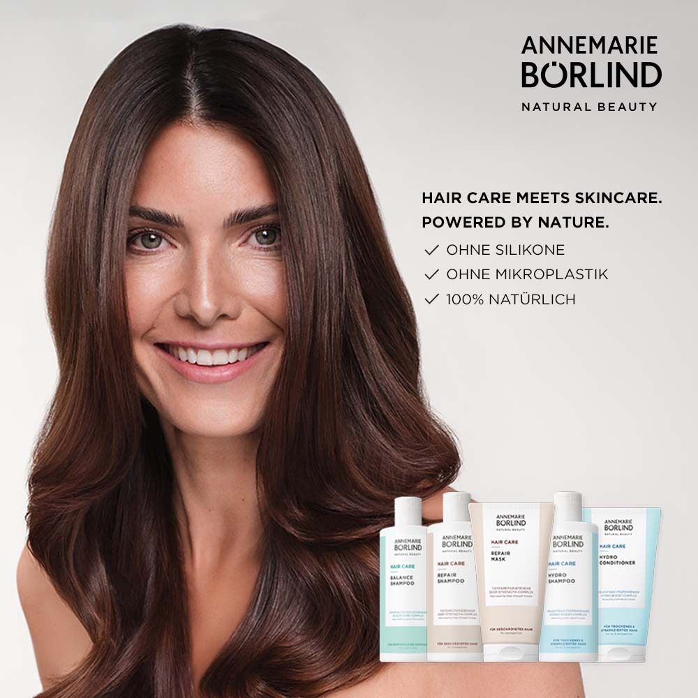 Frau mit langen, braunen Haaren. Produkte der Marke ANNEMARIE BÖRLIND im Hintergrund. Text: HAIR CARE MEETS SKINCARE.