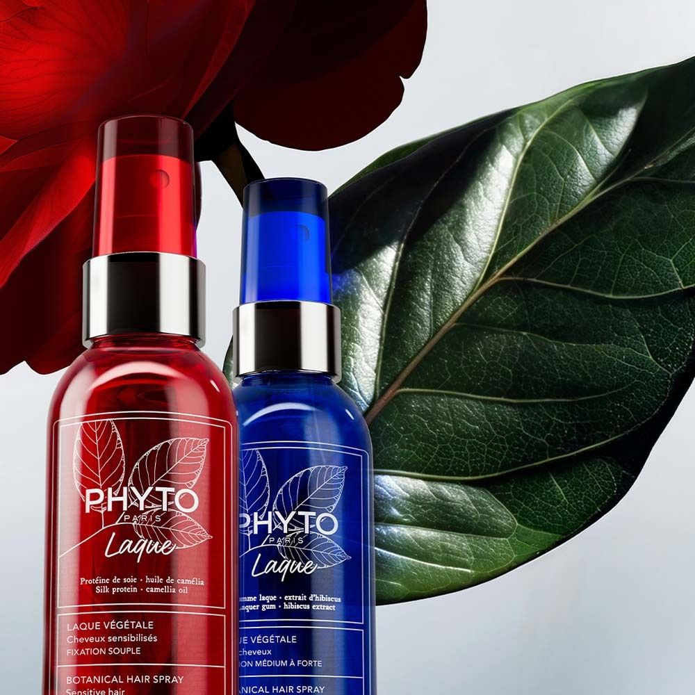 Zwei Sprühflaschen, rot und blau, mit silbernen Verschlüssen. Aufschrift: PHYTO Paris Laque. Botanisches Haarspray. Hintergrund: Blattwerk.